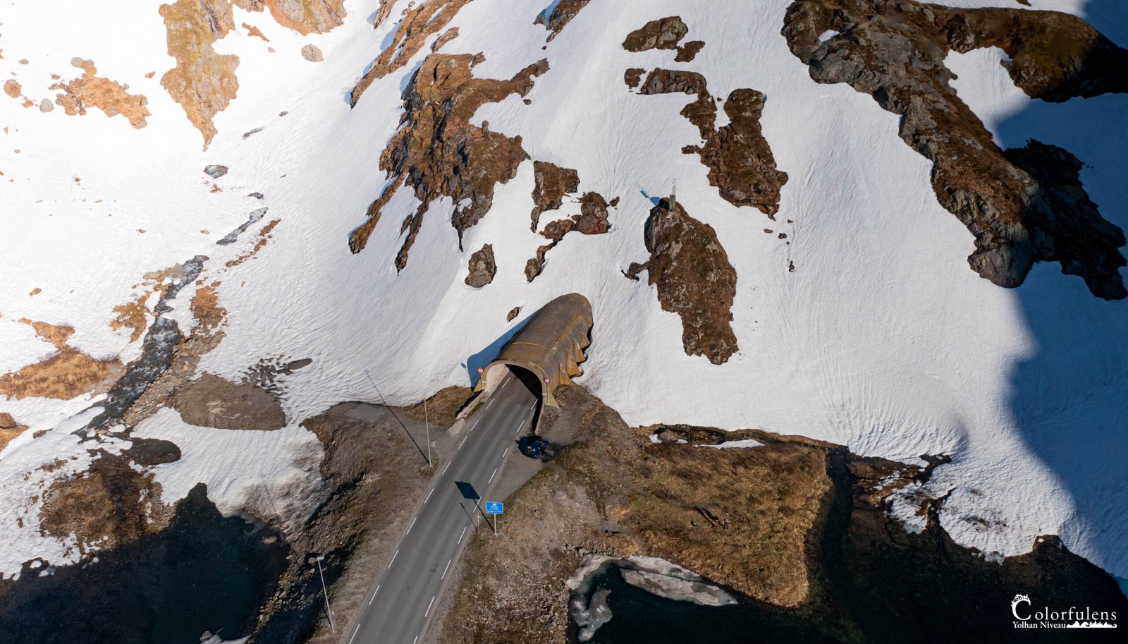 Photo aérienne d'une route traversant un tunnel dans un paysage enneigé de Vestland. La neige, la terre et le tunnel illustrent l'interaction entre nature et architecture.