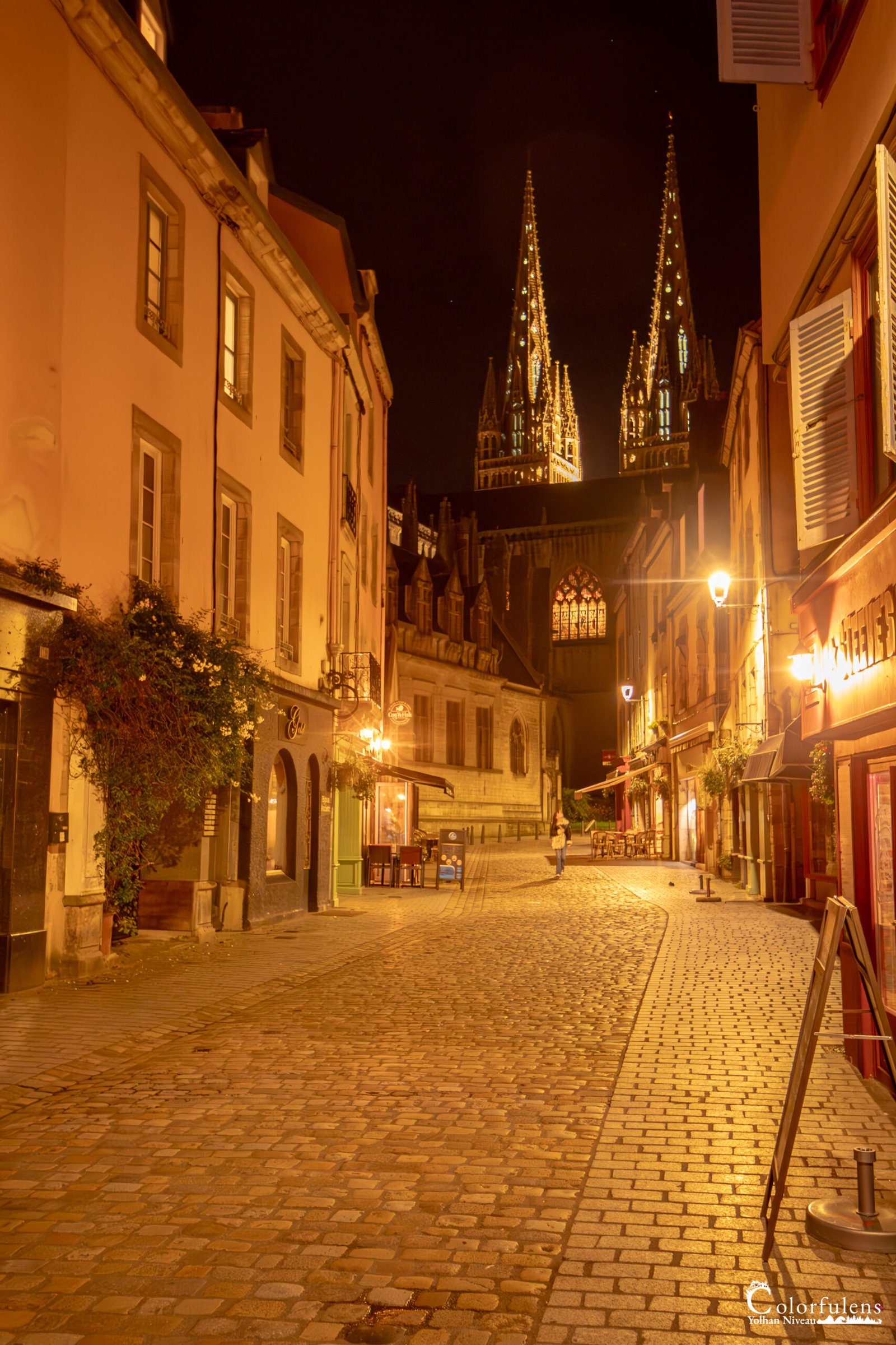 Promenade nocturne dans la ville historique de Quimper, avec la cathédrale illuminée et des réverbères projetant des ombres sur la chaussée.