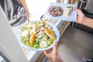 Main servant une assiette de salade gourmande avec légumes, poulet, œuf et fromage, illustrant un plat sain et équilibré en restaurant.