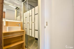 Une salle de bain moderne avec des éléments en bois, un grand miroir et une cabine de douche transparente, offrant élégance et fonctionnalité.