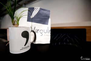 Photographie d'une tasse personnalisée avec motif artistique et inscription poétique à côté d'un sac de boutique "Virgule", ambiance moderne et chaleureuse.