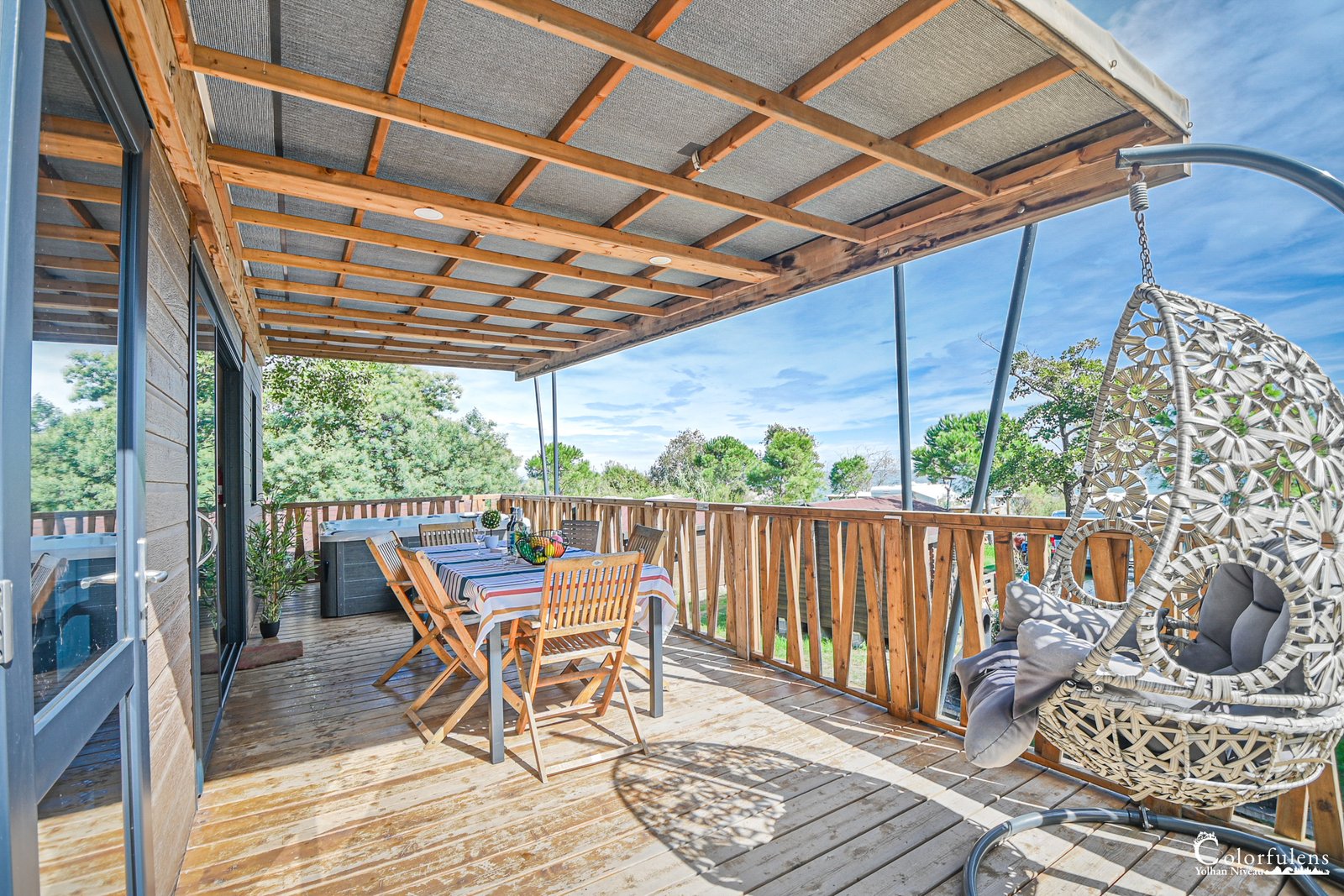 Terrasse en bois d'un mobil-home avec table en bois et fauteuil suspendu dans un camping en Corse, idéale pour la détente et les repas en extérieur.