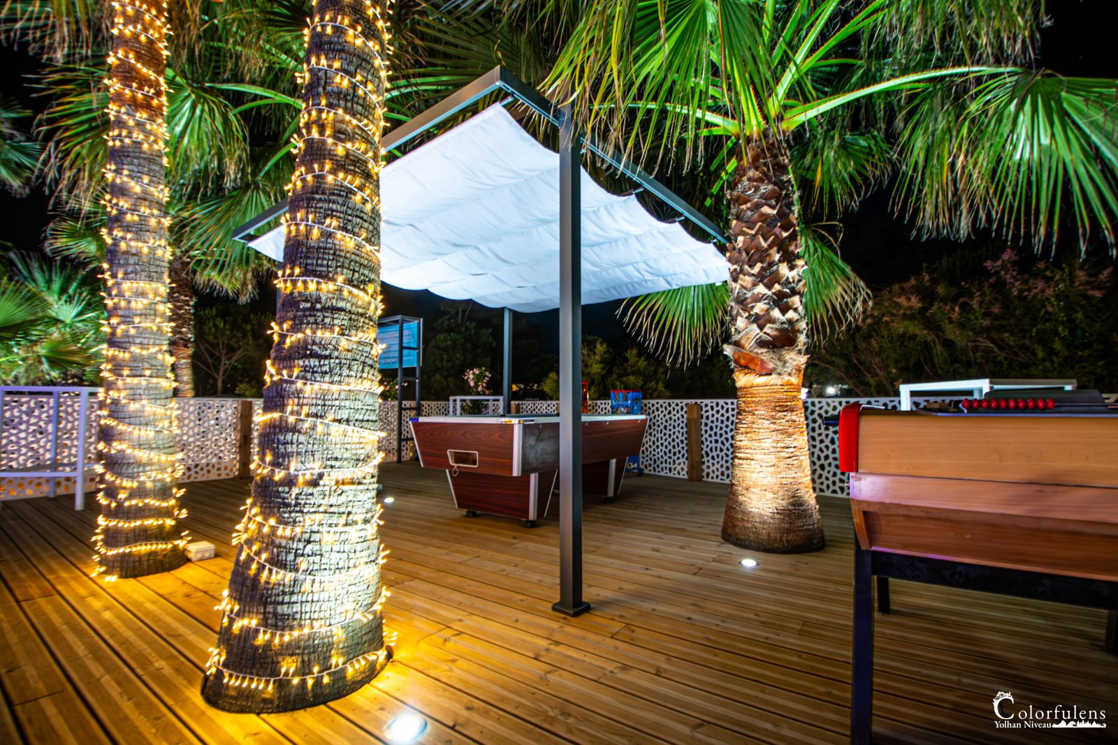 Ambiance festive en terrasse avec lumière douce, palmiers illuminés et baby-foot en Corse