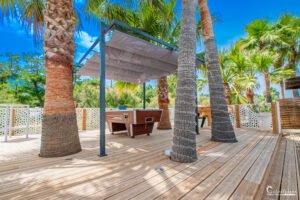 Terrasse en bois entourée de palmiers sous un ciel bleu, évoquant la tranquillité et la relaxation.