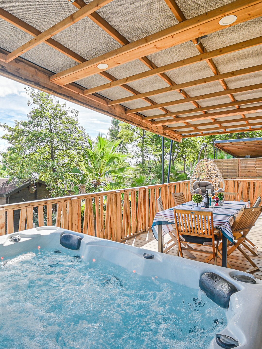 Terrasse en bois avec jacuzzi et table extérieure, offrant une détente inégalée au Camping Merendella, cadre idéal pour se ressourcer