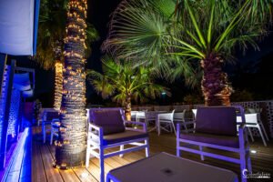 Terrasse nocturne du restaurant Merendella avec éclairage tamisé et palmiers luxuriants, créant une ambiance tropicale et relaxante en Corse.