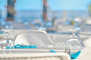 Table dressée sur une terrasse en bord de mer avec verres à vin et couverts raffinés, évoquant l'élégance d'un déjeuner estival.