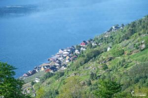 Village pittoresque en bord de lac, avec maisons colorées et nature environnante, sous un soleil radieux.