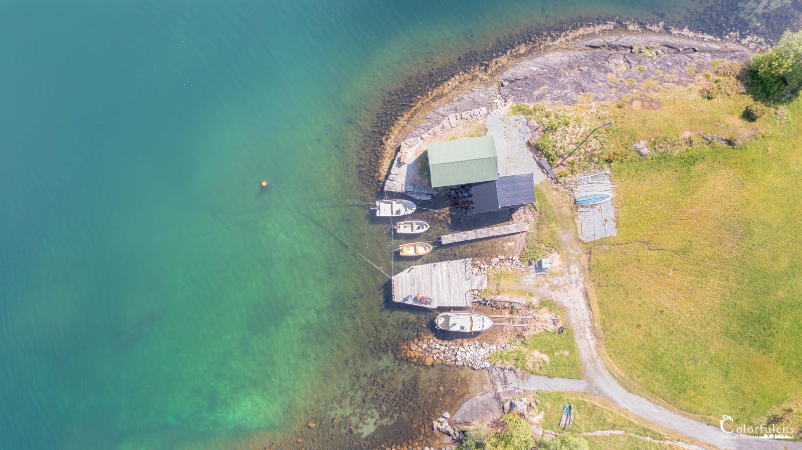 Vue aérienne d'une cabane norvégienne au bord d'un lac, avec des bateaux et une nature majestueuse, inspirant calme et sérénité.