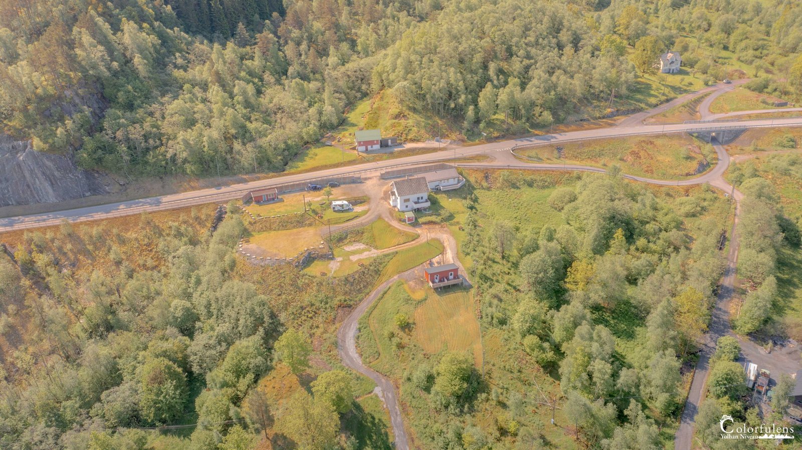 Vue aérienne d'un camping idyllique entouré de nature verdoyante, avec un chemin sinueux soulignant l'harmonie du paysage.