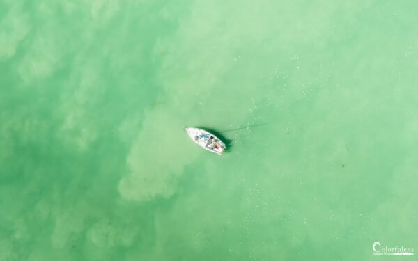 Bateau solitaire flottant sur des eaux vert émeraude calmes, symbole de tranquillité et d'isolement.