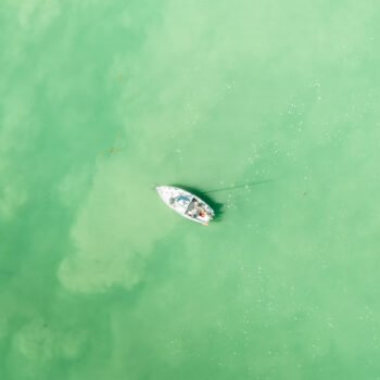 Bateau solitaire flottant sur des eaux vert émeraude calmes, symbole de tranquillité et d'isolement.