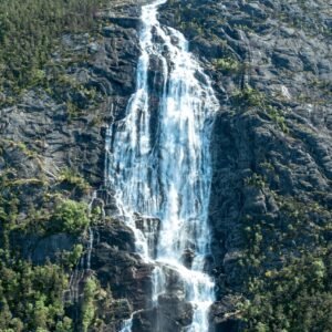 Cascade déferlante sur roche escarpée, entourée de verdure dense. Lumière solaire illuminant les gouttelettes en suspension.