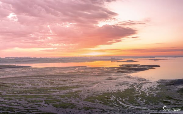 Coucher de soleil sur la Grande Grève en Finistère, illuminant le paysage marin de teintes roses et orangées, avec des reflets sur l'eau, capturant un moment de tranquillité typique de la côte bretonne.