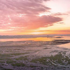 Coucher de soleil sur la Grande Grève en Finistère, illuminant le paysage marin de teintes roses et orangées, avec des reflets sur l'eau, capturant un moment de tranquillité typique de la côte bretonne.