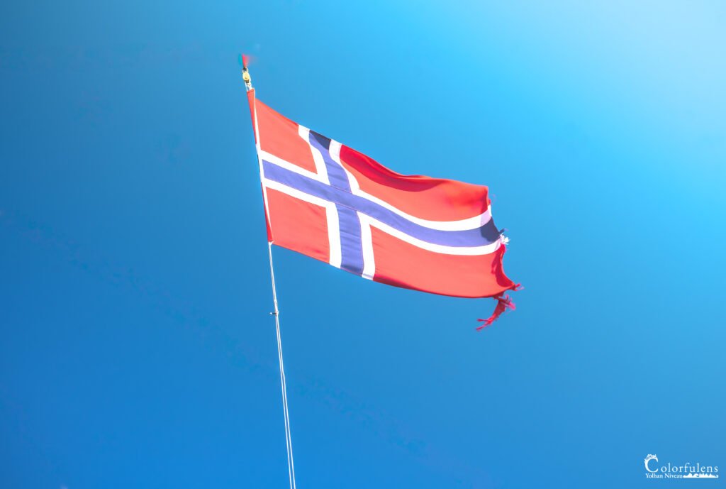 Drapeau norvégien flottant au vent sur fond de ciel bleu, symbolisant fierté et liberté nationales.