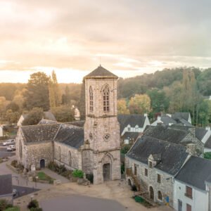 Vue aérienne d'une église au cœur d'un village français entouré de verdure et baigné de lumière au lever du soleil.