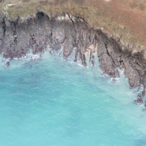 Image aérienne des falaises de la Pointe du Groin en Bretagne, où le gris des roches contraste avec le bleu turquoise de l'océan.