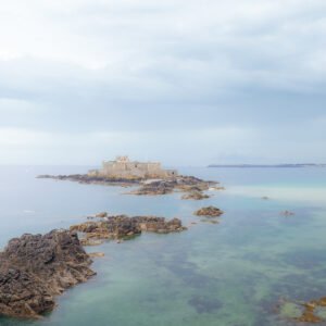 Le Fort National de Saint-Malo émerge entouré par les eaux claires et les rochers, révélant un paysage breton captivant et historique.