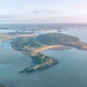 Vue aérienne de l'île de Berder enveloppée dans la brume matinale, capturant la tranquillité et le mystère de la Bretagne avec des voiliers paisibles à l'ancre.