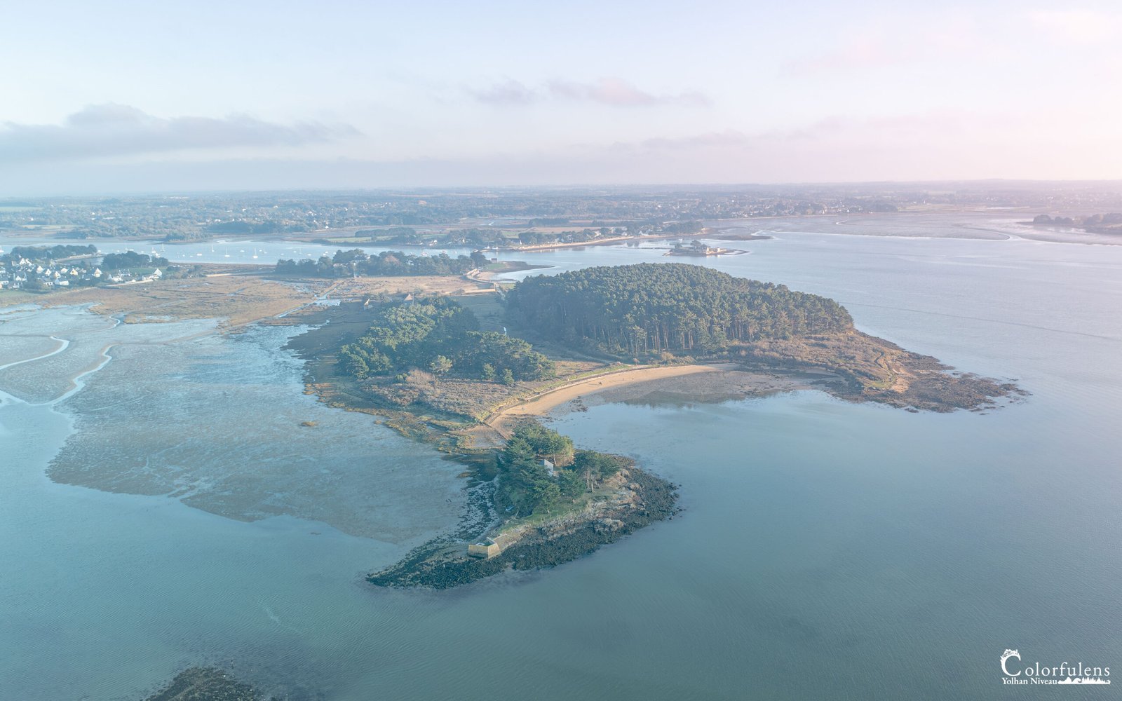 Vue aérienne de l'île de Berder enveloppée dans la brume matinale, capturant la tranquillité et le mystère de la Bretagne avec des voiliers paisibles à l'ancre.