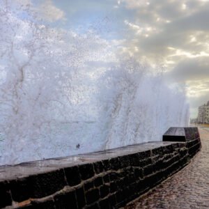 Cette photographie captivante montre une grande vague frappant la promenade de Saint-Malo, illustrant la puissance de la mer durant la marée haute.