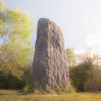Menhir mystérieux baigné dans une lumière matinale en forêt bretonne, éveillant légendes et respect