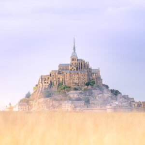 Le Mont Saint-Michel se dresse majestueusement dans une mer de brume matinale, surplombant un champ doré, créant une scène à couper le souffle qui témoigne de son histoire.