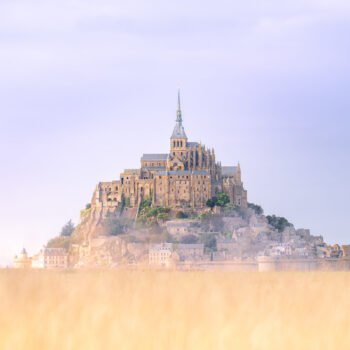 Le Mont Saint-Michel se dresse majestueusement dans une mer de brume matinale, surplombant un champ doré, créant une scène à couper le souffle qui témoigne de son histoire.