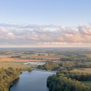 Vue aérienne d'un paysage de campagne au crépuscule avec un plan d'eau, des arbres et des nuages réfléchissant les dernières lueurs du jour.