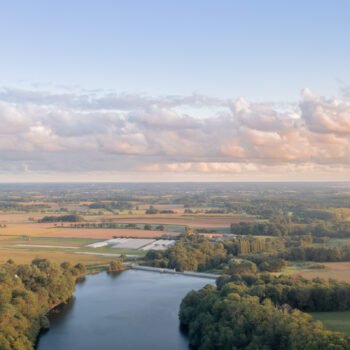 Vue aérienne d'un paysage de campagne au crépuscule avec un plan d'eau, des arbres et des nuages réfléchissant les dernières lueurs du jour.