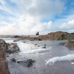 Cette image montre une plage rocheuse paisible sous un ciel nuageux, avec des reflets scintillants sur l'eau qui créent une atmosphère sereine et naturelle.