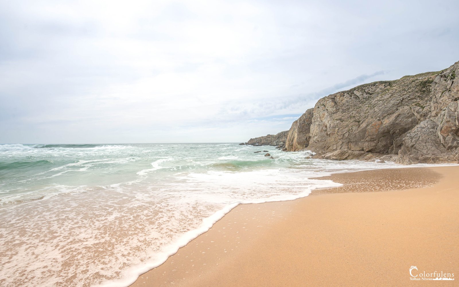 Plage sauvage de Quiberon sous un ciel nuageux en Bretagne, montrant des nuages épars avec des falaises imposantes sur le rivage.