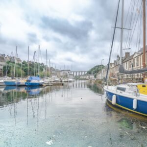 Un port calme avec voiliers amarrés à Morlaix, reflétant l'histoire et la tranquillité sous un ciel nuageux.