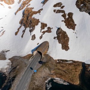 Photo aérienne d'une route traversant un tunnel dans un paysage enneigé de Vestland. La neige, la terre et le tunnel illustrent l'interaction entre nature et architecture.