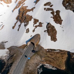 Photo aérienne d'une route traversant un tunnel dans un paysage enneigé de Vestland. La neige, la terre et le tunnel illustrent l'interaction entre nature et architecture.
