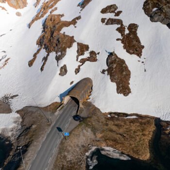 Photo aérienne d'une route traversant un tunnel dans un paysage enneigé de Vestland. La neige, la terre et le tunnel illustrent l'interaction entre nature et architecture.