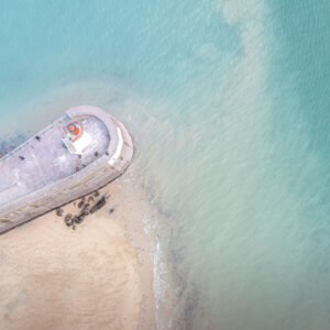 Vue aérienne d'un phare coloré sur une jetée avec des eaux turquoises en arrière-plan, symbolisant la protection côtière et l'inspiration maritime.