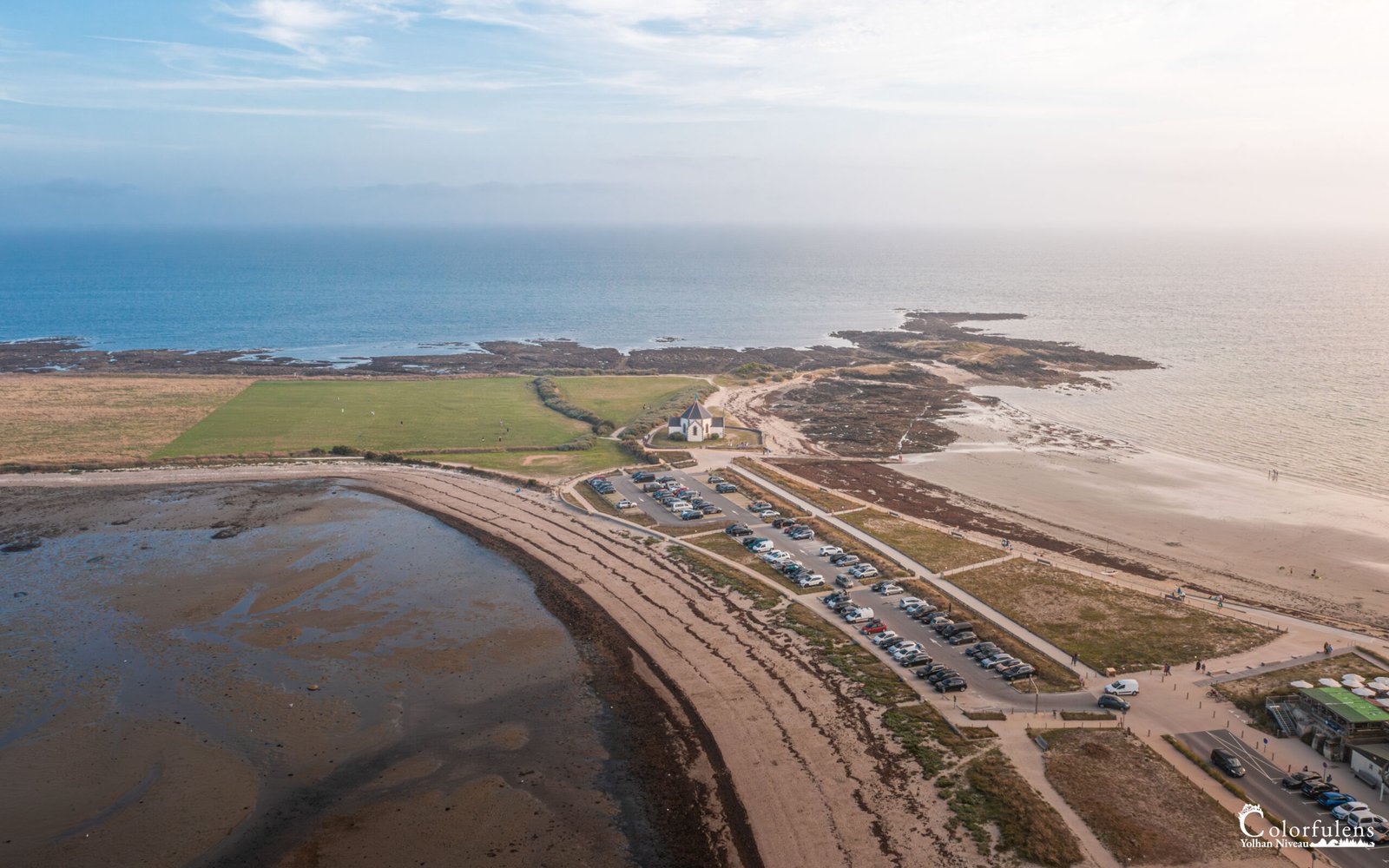 Vue aérienne saisissante de la plage de Penvins, illustration de la beauté tranquille de la côte bretonne, avec chapelle isolée et routes côtières invitant à l'évasion.