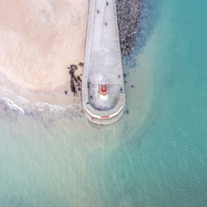 Vue aérienne spectaculaire du Phare des Môles des Noirs à Saint-Malo, entouré d'un paysage marin paisible, mettant en valeur la plage de sable et l'architecture emblématique du phare.