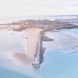 Vue aérienne de Saint-Malo avec son phare emblématique et les plages de Bretagne, illustrant le charme et la tranquillité du paysage marin.