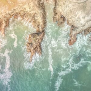 Vue aérienne époustouflante montrant les vagues dynamiques s'écrasant contre les rochers robustes de la côte de Quiberon, illustrant la force impressionnante de la nature bretonne.