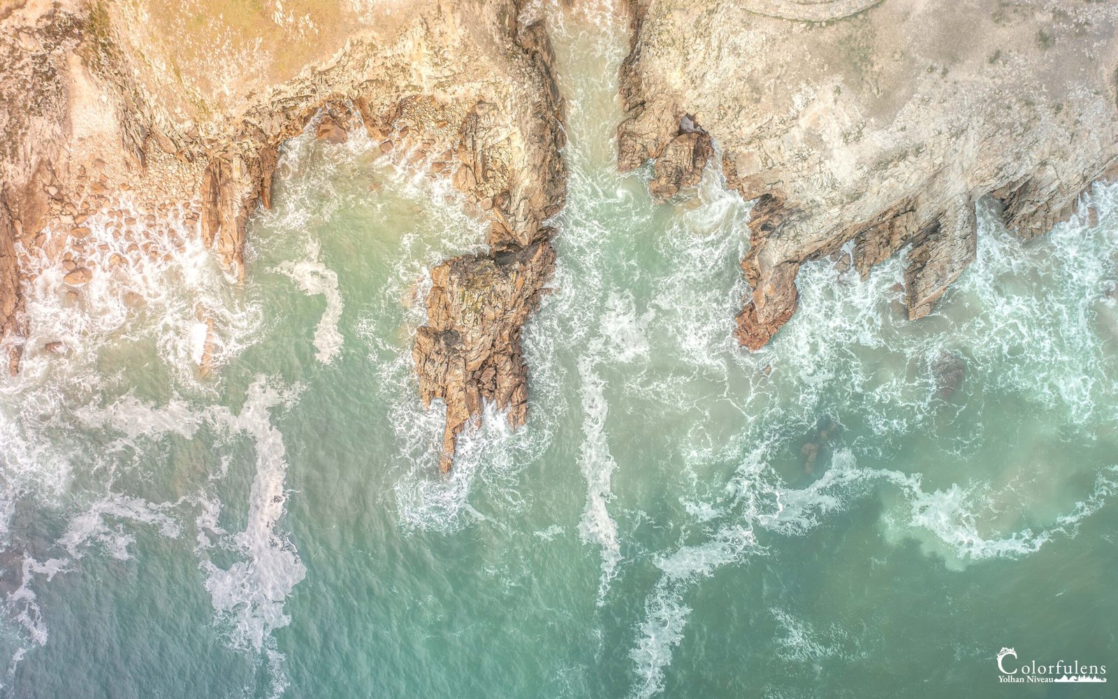 Vue aérienne époustouflante montrant les vagues dynamiques s'écrasant contre les rochers robustes de la côte de Quiberon, illustrant la force impressionnante de la nature bretonne.